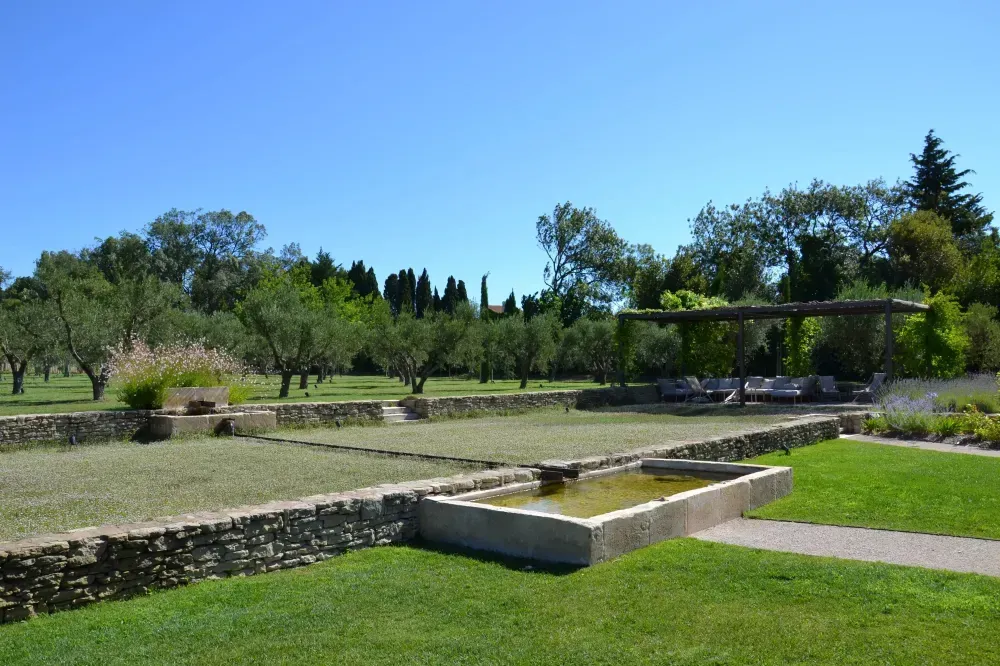Jardin ensoleillé avec un mur de soutènement en pierre, une pelouse verdoyante et des arbres sous un ciel bleu dégagé