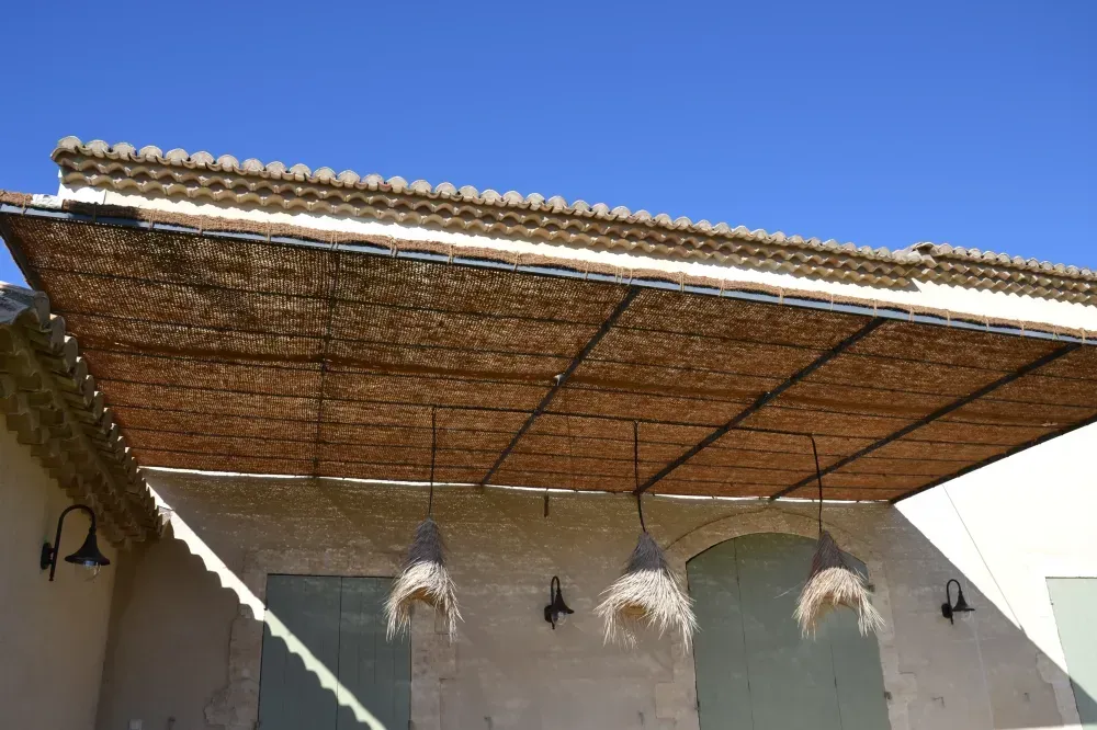 Auvent en roseaux au-dessus d’un patio, avec des plantes suspendues et des murs blancs sous un ciel bleu