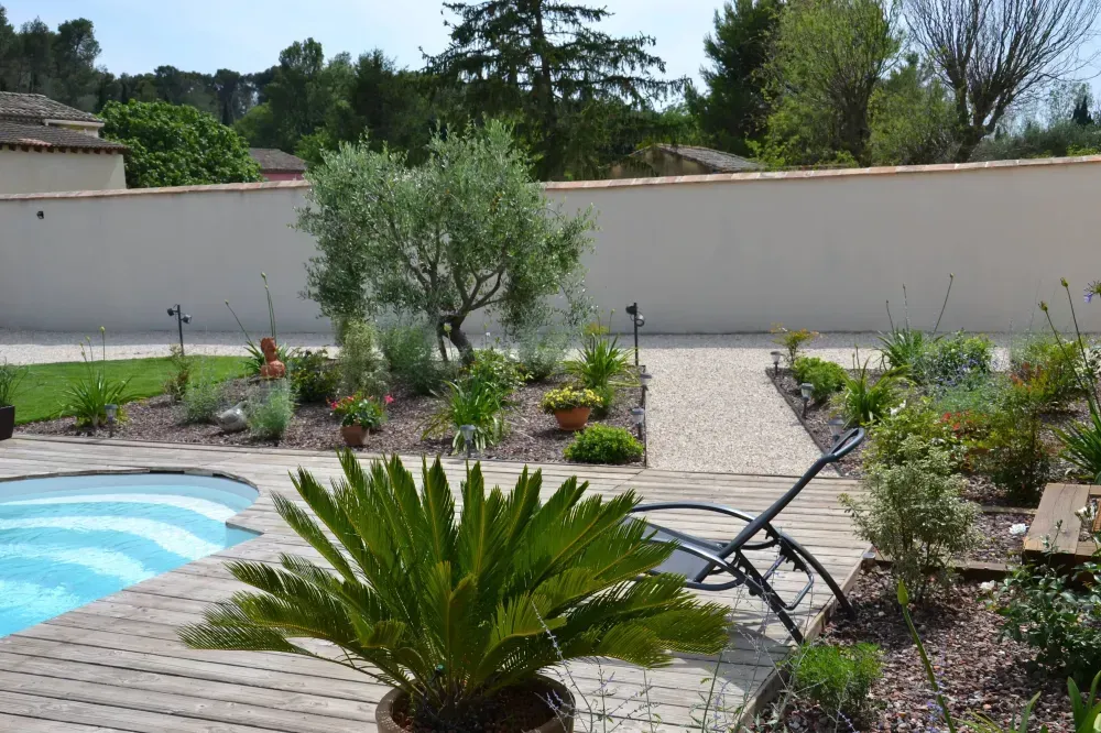 Piscine et terrasse dans un jardin, avec des chaises longues, des plantes en pot et un mur blanc préservant l’intimité