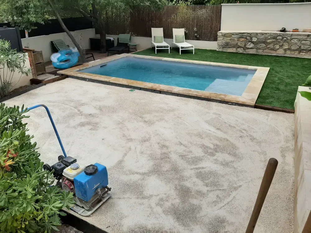 Patio dans le jardin avec une piscine rectangulaire, du gazon synthétique, des chaises longues et un mur de soutènement en pierre