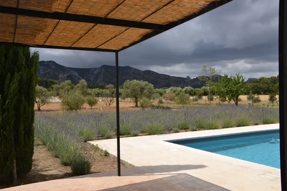 Patio couvert au bord d’une piscine, avec un paysage désertique et des montagnes orageuses au loin