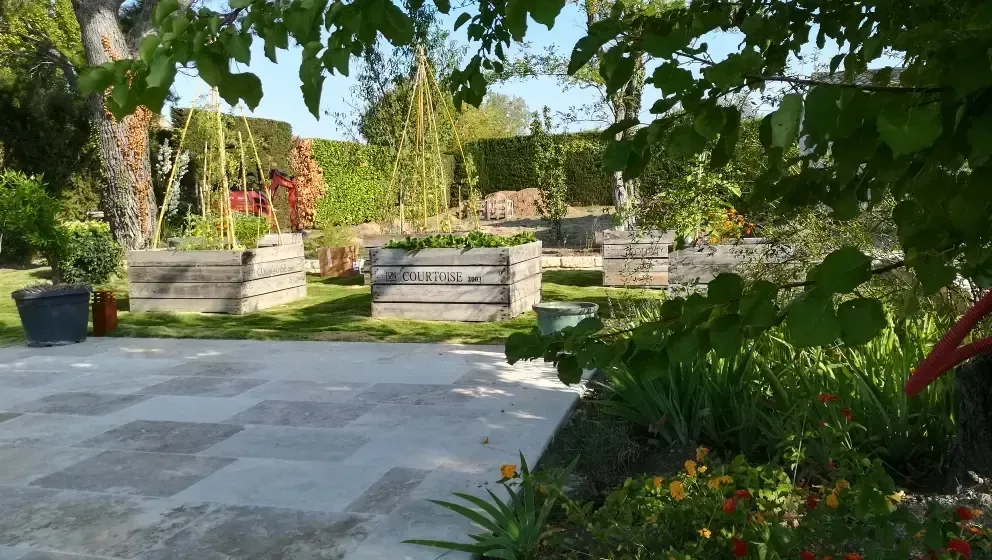 Patio de jardin ensoleillé avec des marches en pierre, une végétation luxuriante et des massifs de fleurs près d’une terrasse dallée