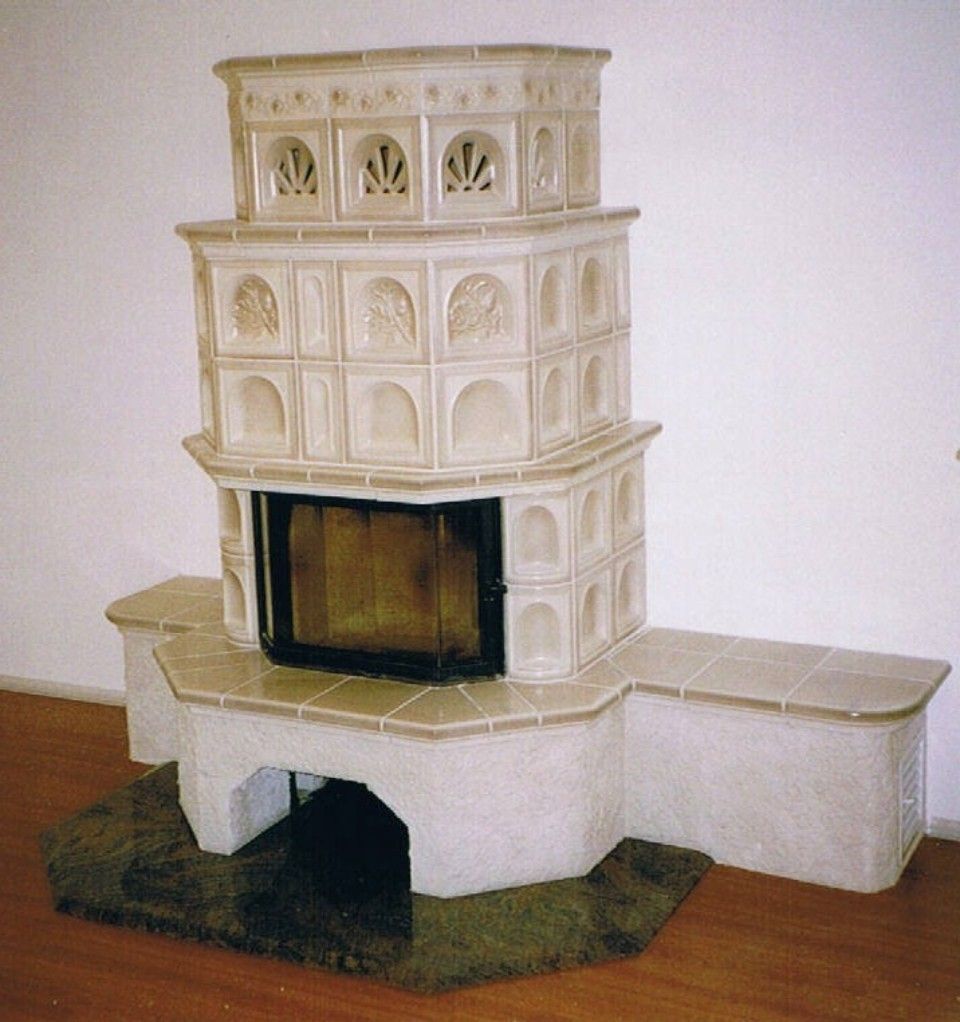 Kachelofen mit verzierten Kacheln in Creme und sichtbarer Feuerstelle hinter Sicherheitsglas