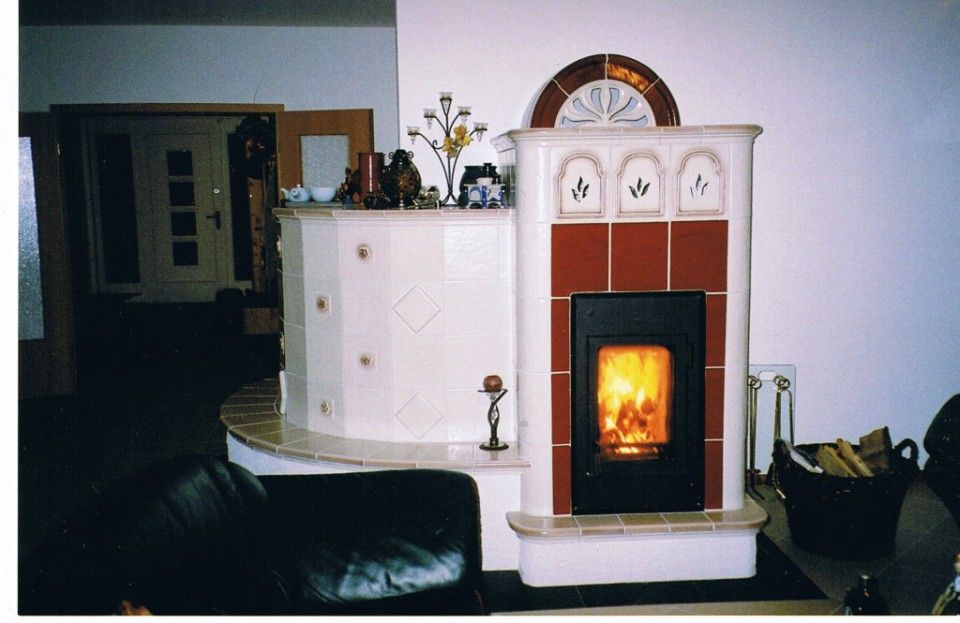 Kachelofen im Wohnzimmer, der um die Ecke geht mit umlaufender Sitzbank und sichtbarer Feuerstelle