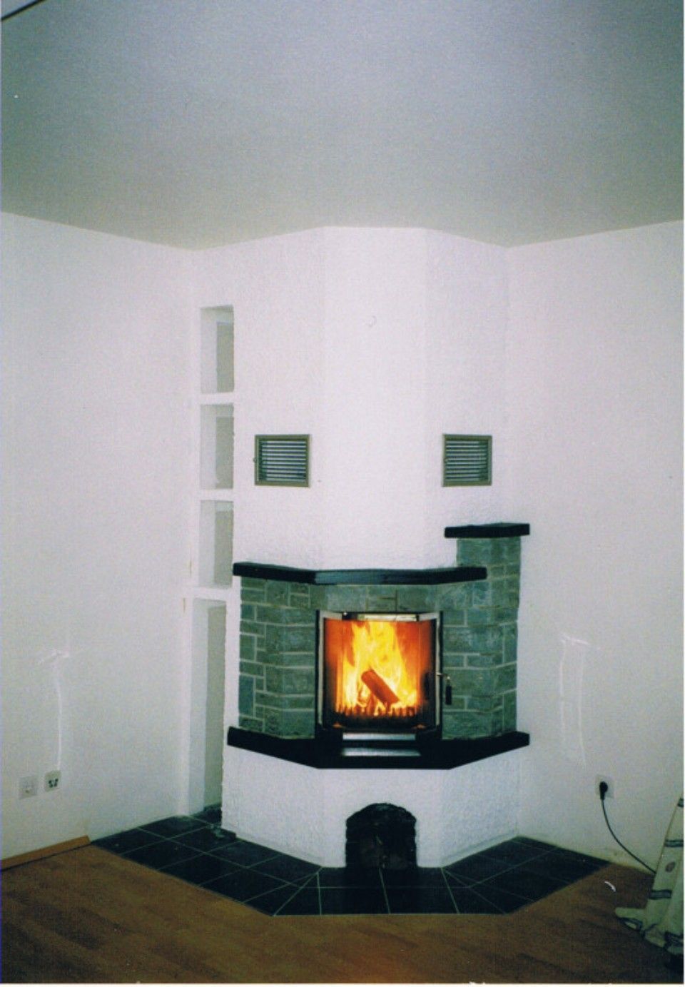 Kaminofen in der Zimmerecke mit verbauten Schornstein und um die Feuerstelle Steinverblendung