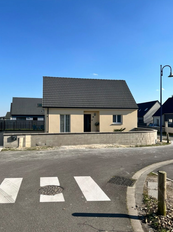 Maison beige au toit noir dans un quartier résidentiel, vue depuis une rue avec un passage piéton.