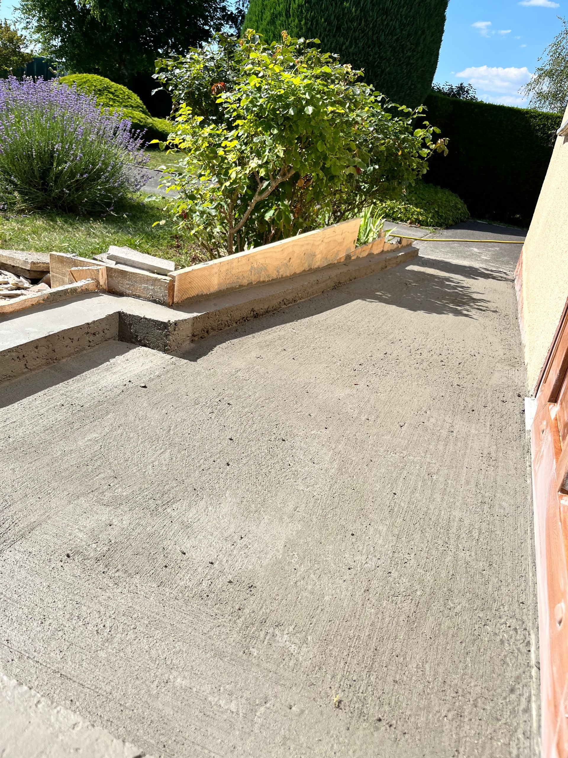 Terrasse en béton avec parterres surélevés et verdure, journée ensoleillée.