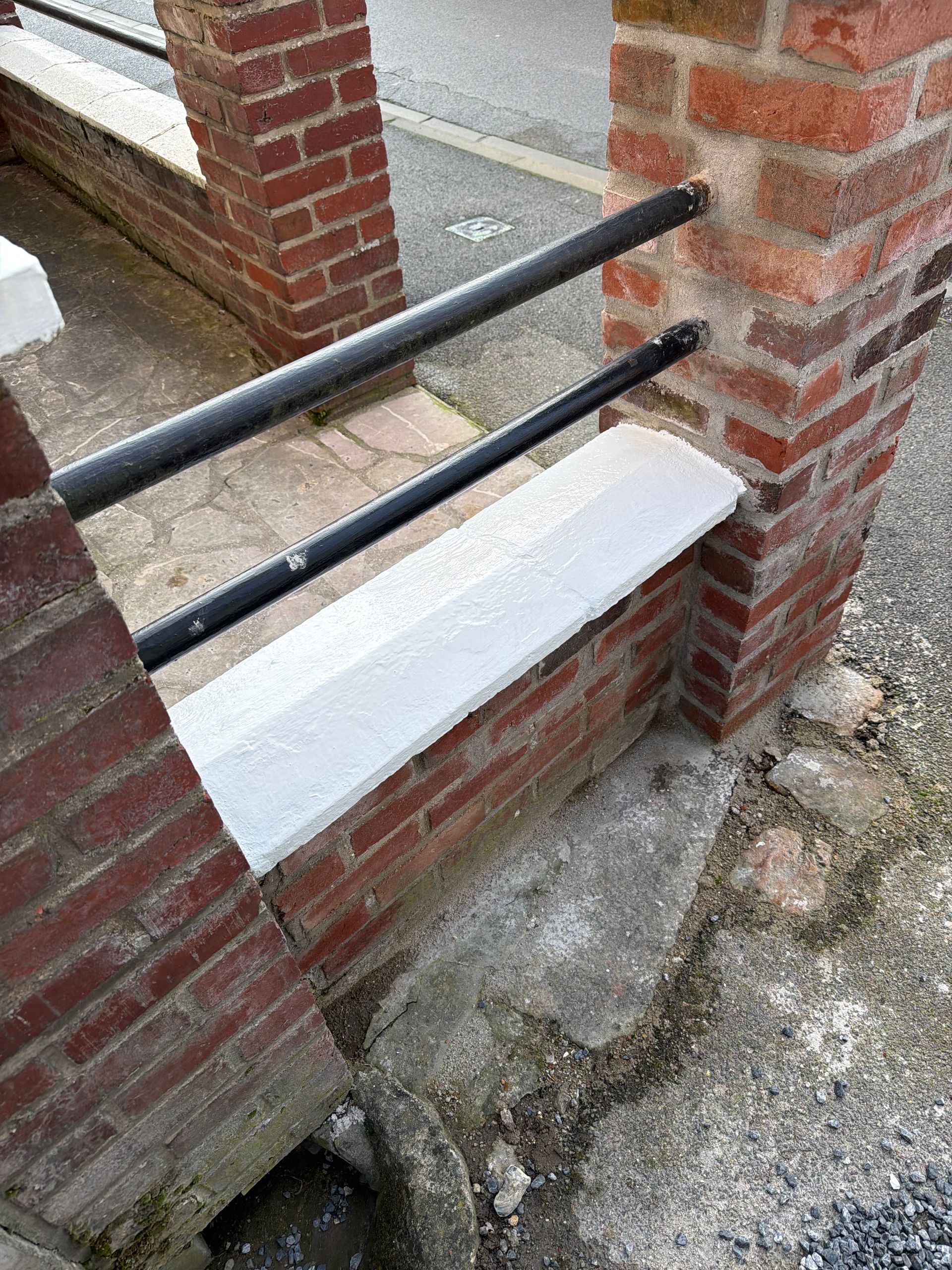 Mur en briques avec une corniche blanche et des mains courantes en métal noir.