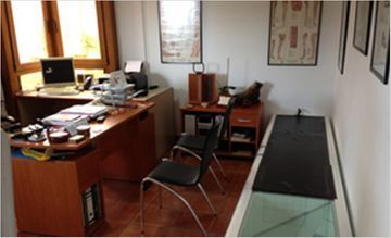Oficina con escritorio, ordenador, silla y cuadros enmarcados en la pared.
