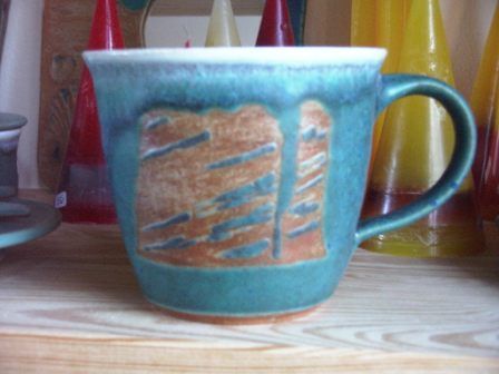 Ein grüner Becher steht auf einem Holztisch mit Kerzen im Hintergrund