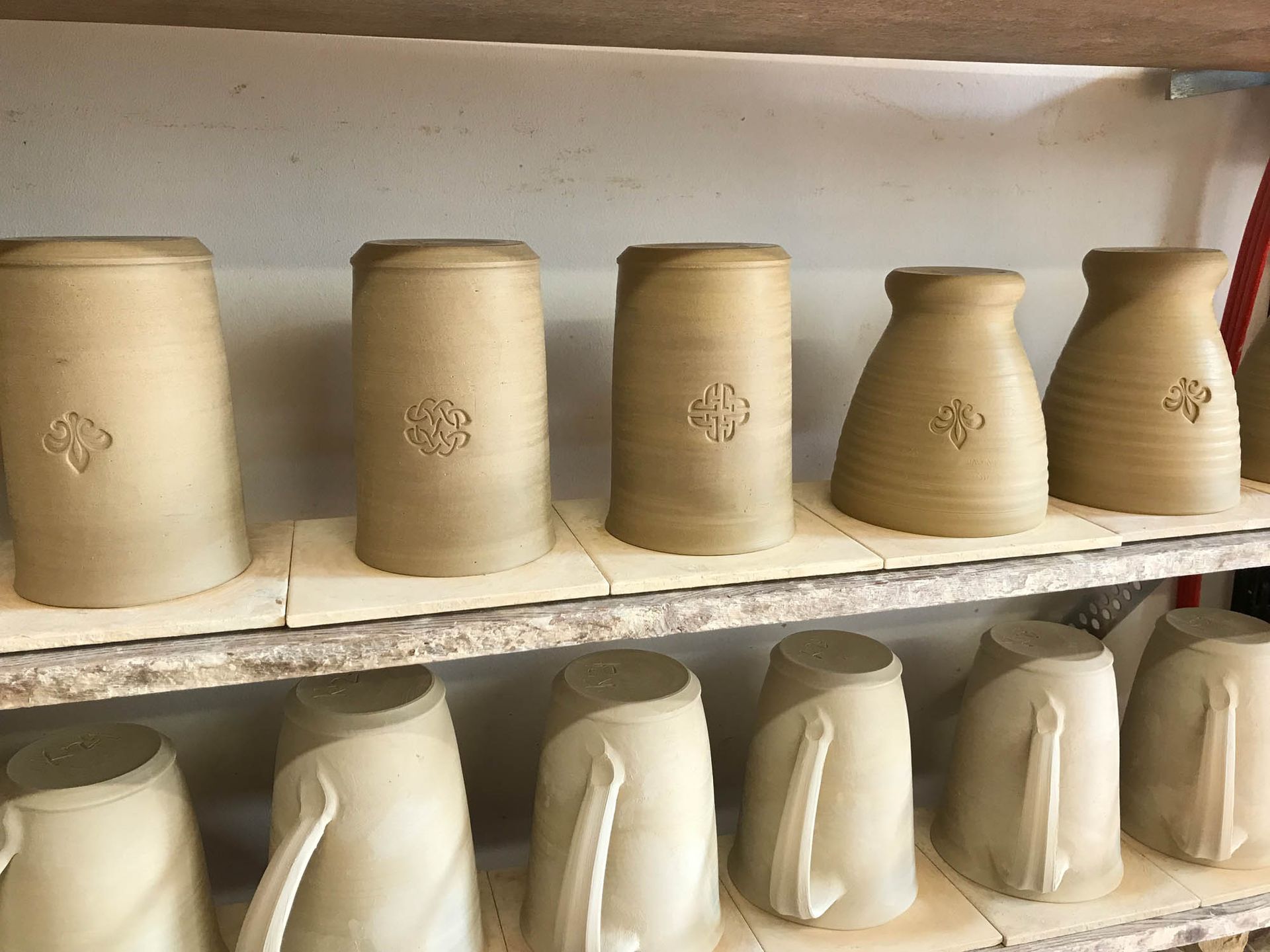 Eine Reihe von Tonkrügen steht auf einem Holzregal.