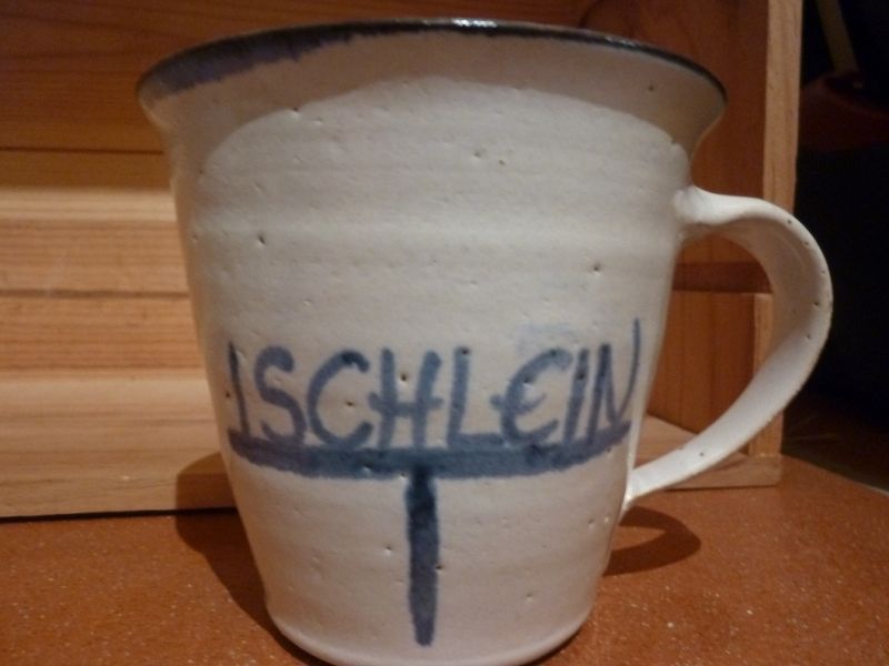 Eine weiße Tasse mit dem Wort „Schlein“ darauf gemalt