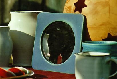 Ein Bilderrahmen mit einer Kerze darin ist von Vasen und Tassen umgeben