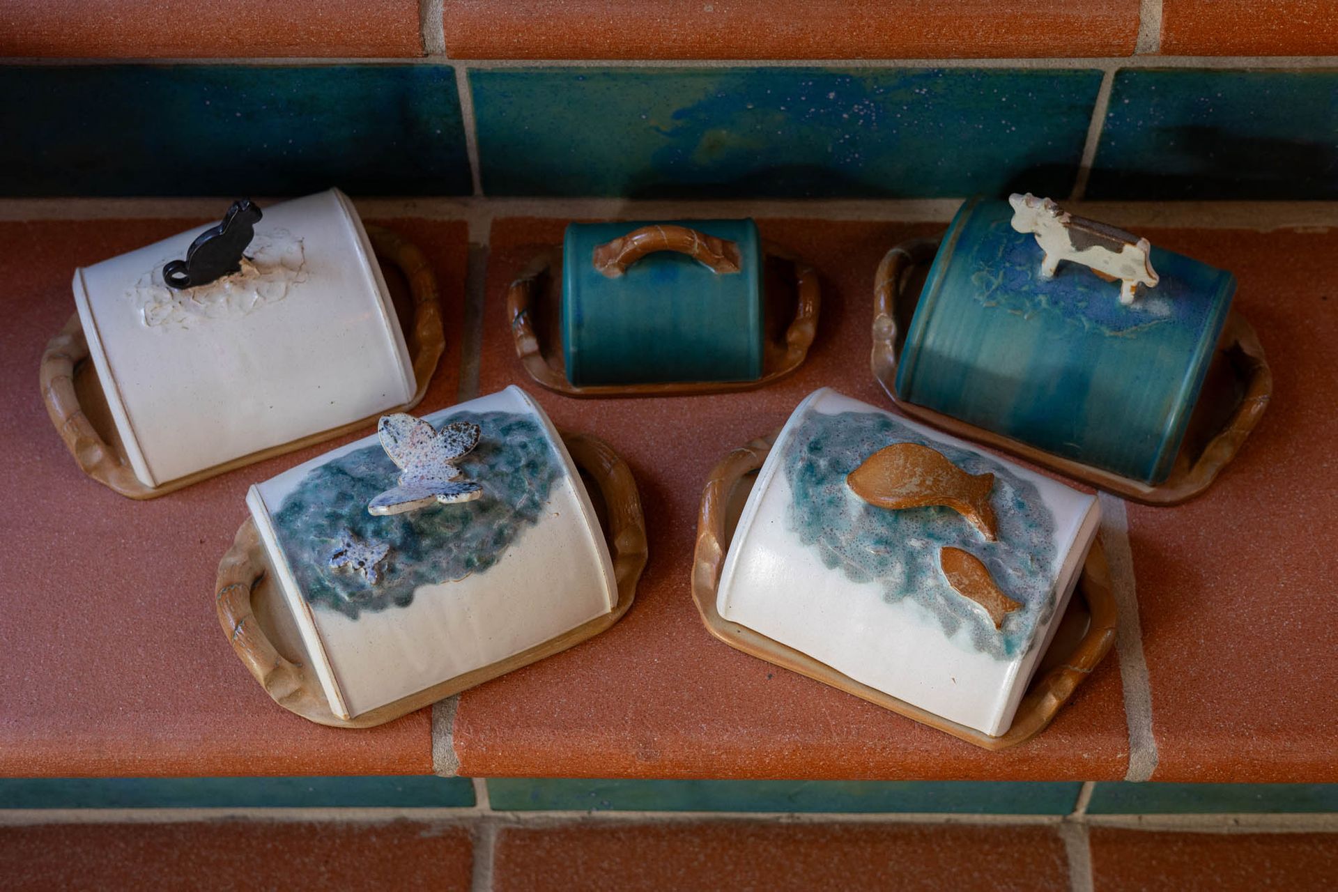 Eine Gruppe von Butterdosen aus Keramik steht auf einem gemauerten Regal.