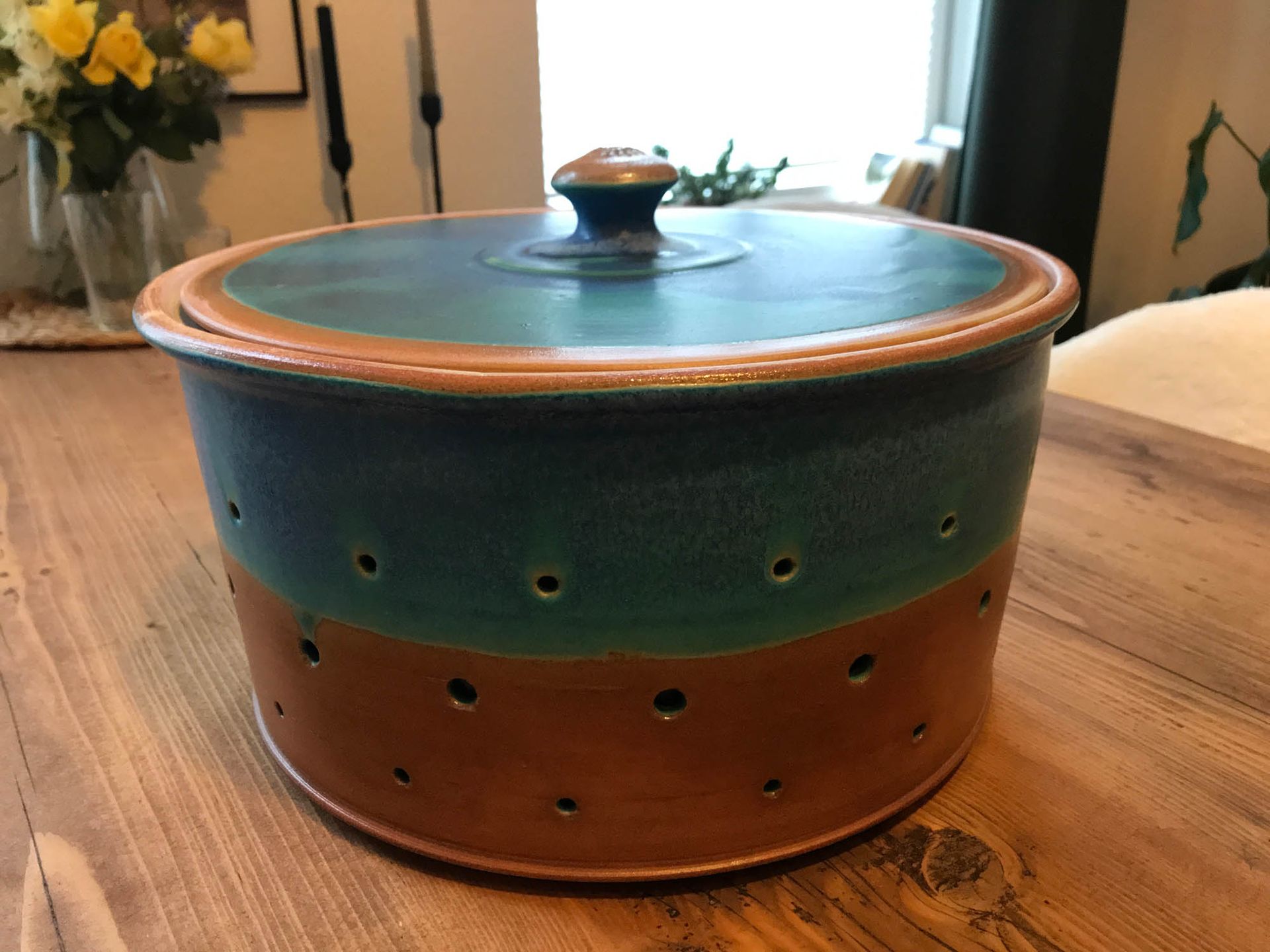 Auf einem Holztisch steht ein blau-brauner Topf mit Löchern.