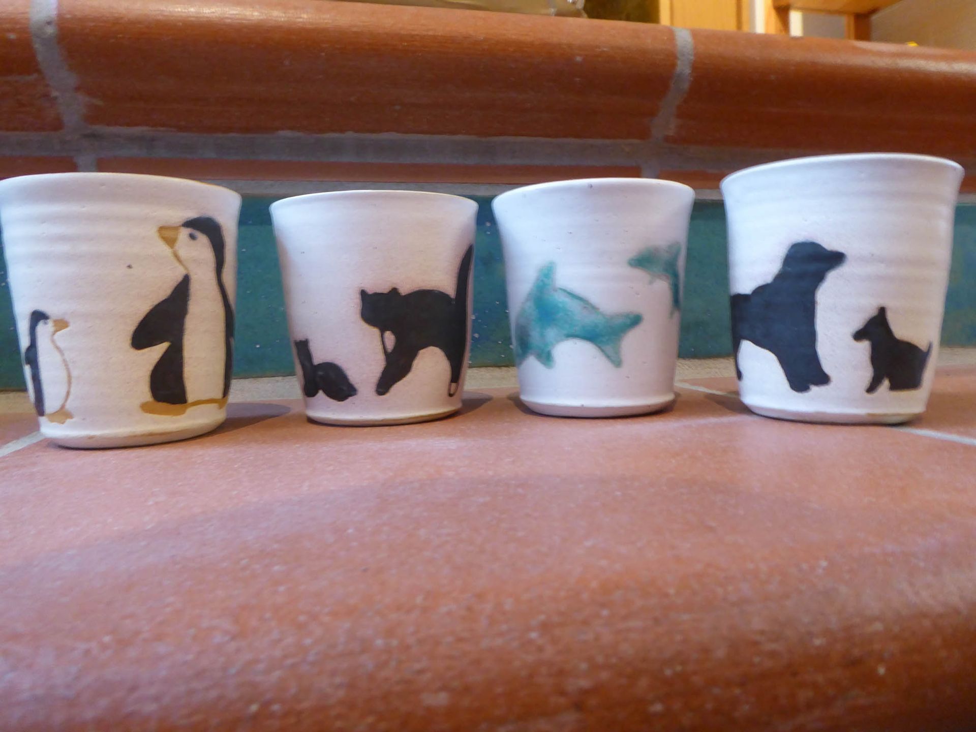 Vier Tassen mit Tieren darauf stehen aufgereiht auf einem Tisch