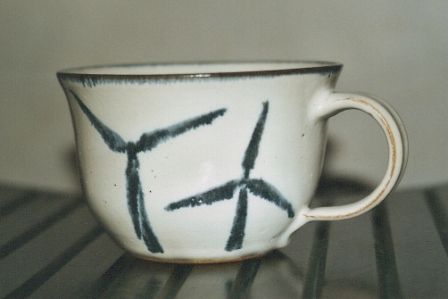 Auf einem Tisch steht eine weiße Tasse mit schwarzen Linien.