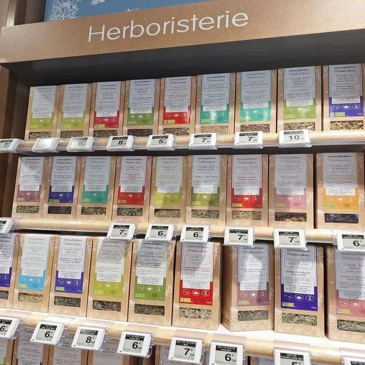 Étagère d'herboristerie avec des rangées de sachets de tisane colorés étiquetés et des étiquettes de prix.
