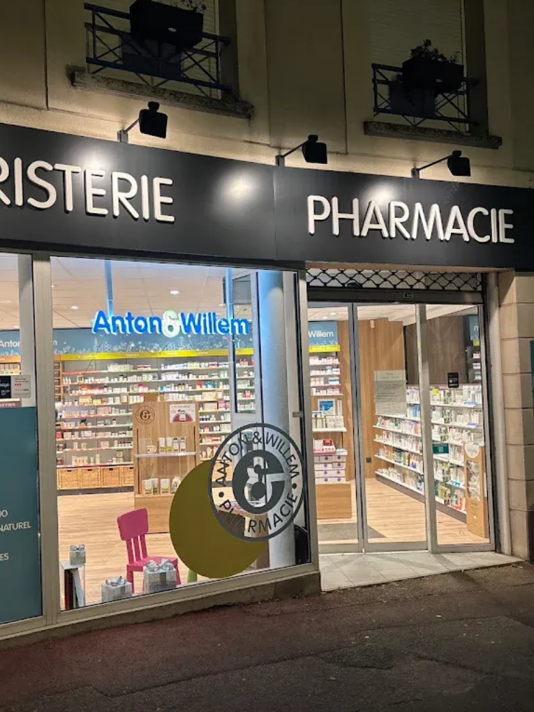 Vue nocturne de la façade d'une pharmacie avec des étagères éclairées et une entrée vitrée.