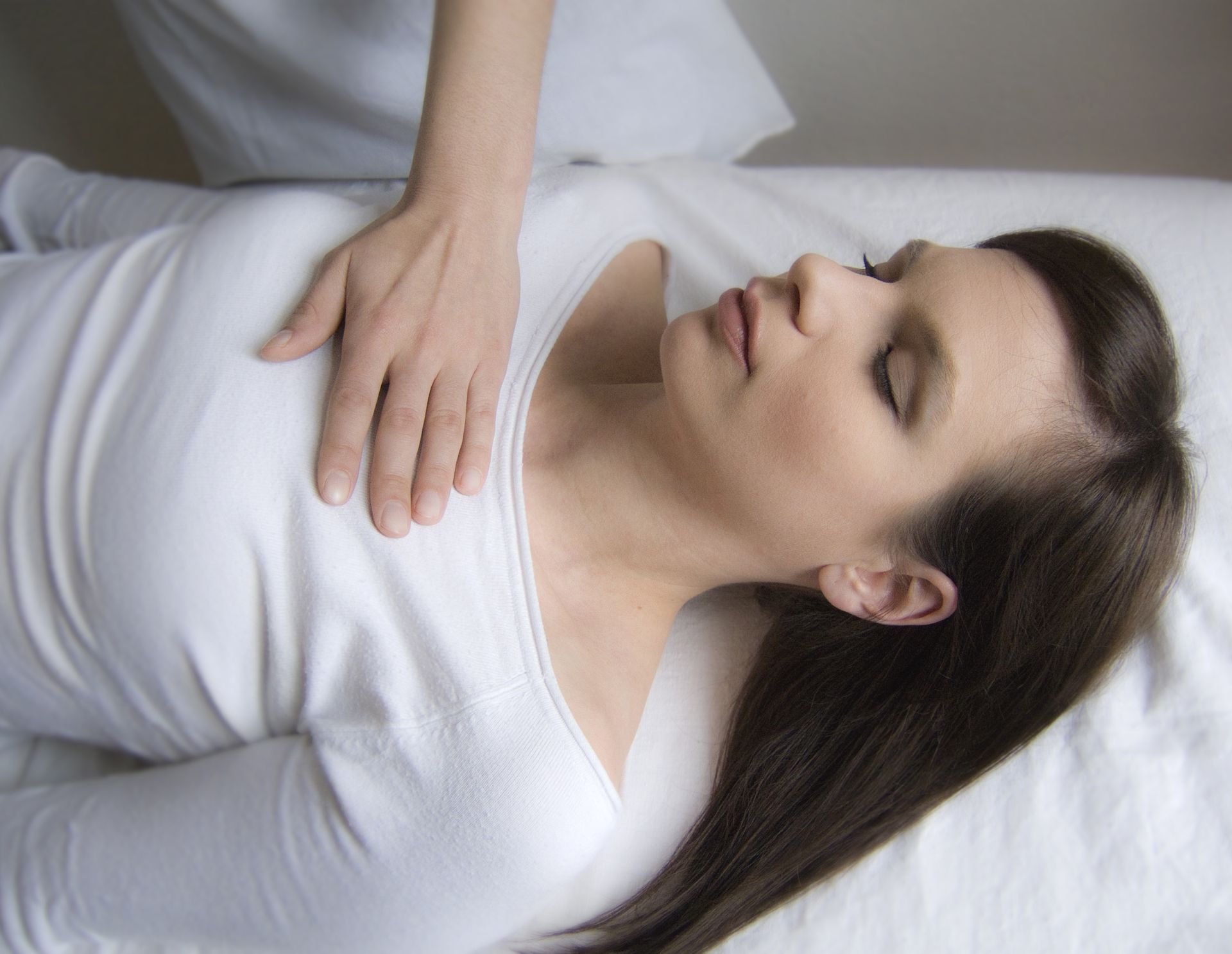 Craniosacrale Körperbehandlung: Person liegt mit geschlossenen Augen auf einer weißen Liege. Hand sanft auf dem Brustkorb.