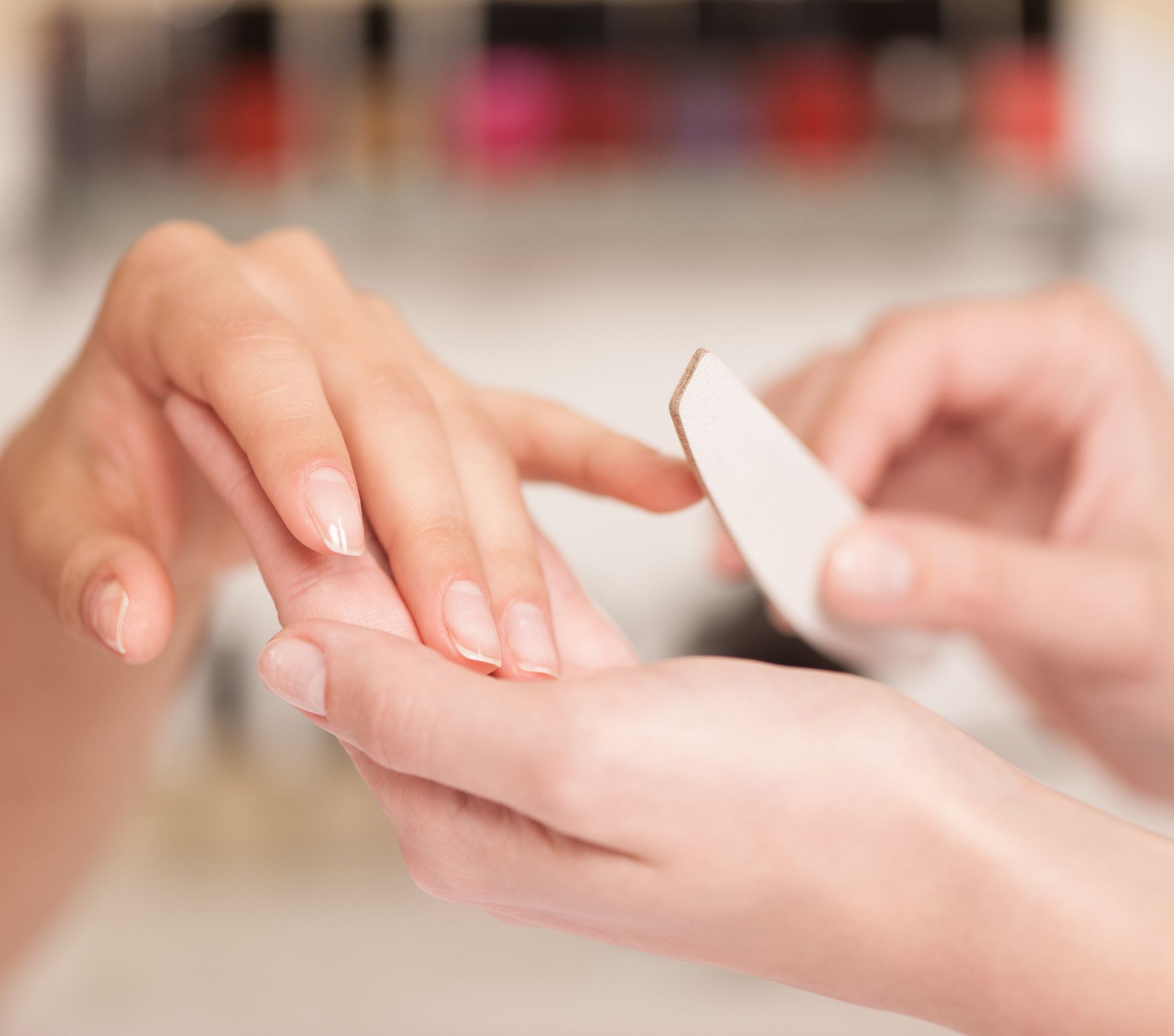 Hände bei der Maniküre, Nagelfeile im Einsatz, Salon-Atmosphäre.