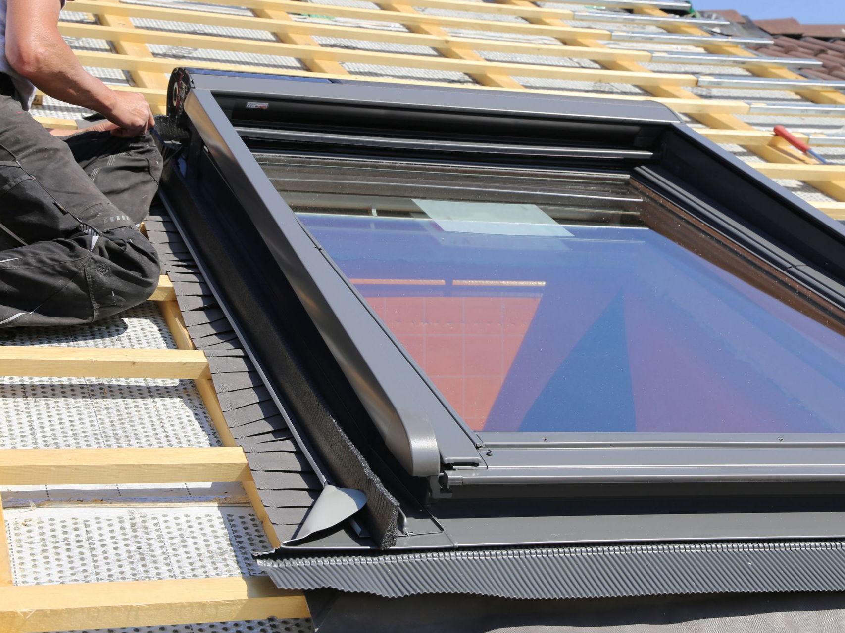 Fenêtre de toit avec un professionnel assis à côté et les liteaux de toiture visibles.