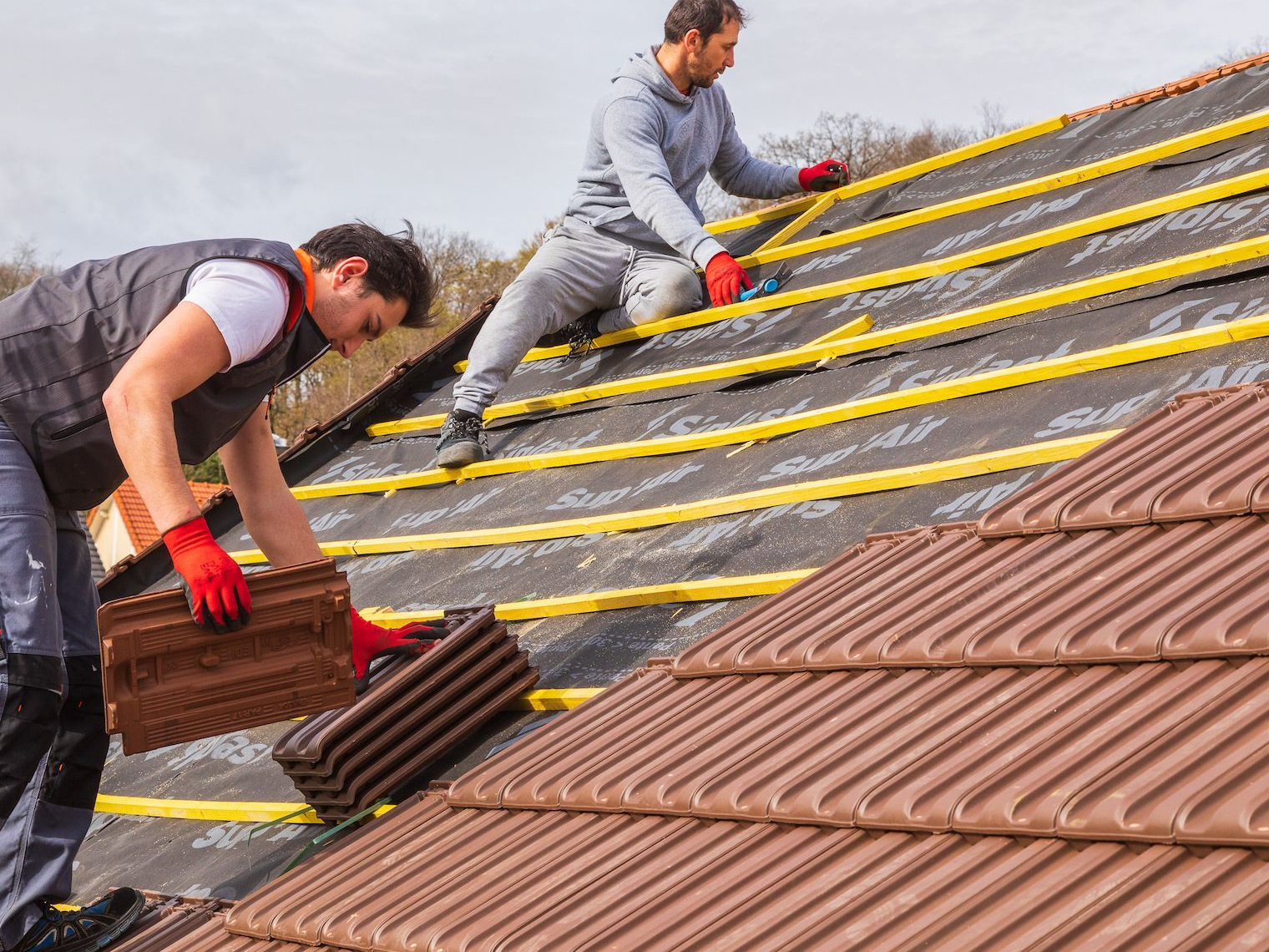 Deux professionnels sur le toit en train de poser les tuiles.