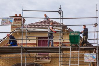 Les professionnels sur un échafaudage devant une maison.