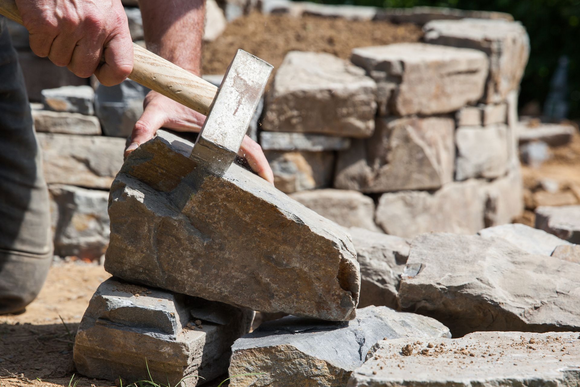 Ein Mann hält einen Hammer über einen Steinhaufen.