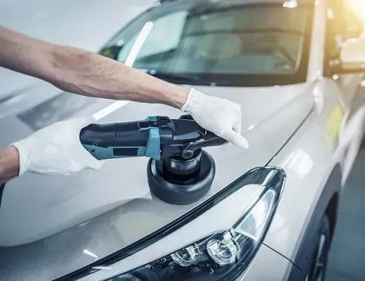 Un hombre está puliendo un coche blanco con una máquina.