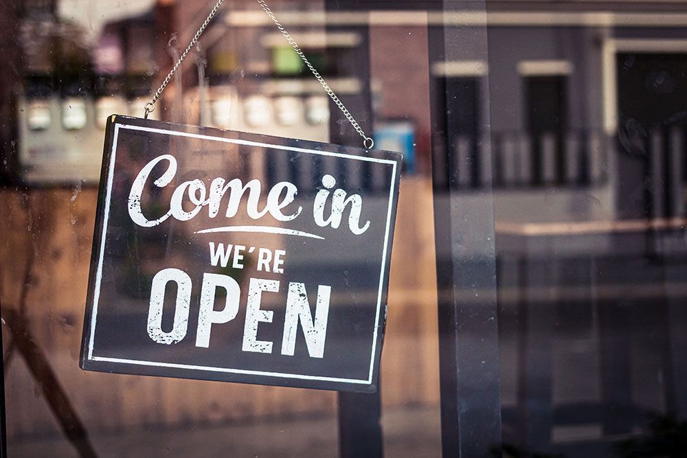 In einem Fenster hängt ein Schild mit der Aufschrift „Kommen Sie herein, wir haben geöffnet“.