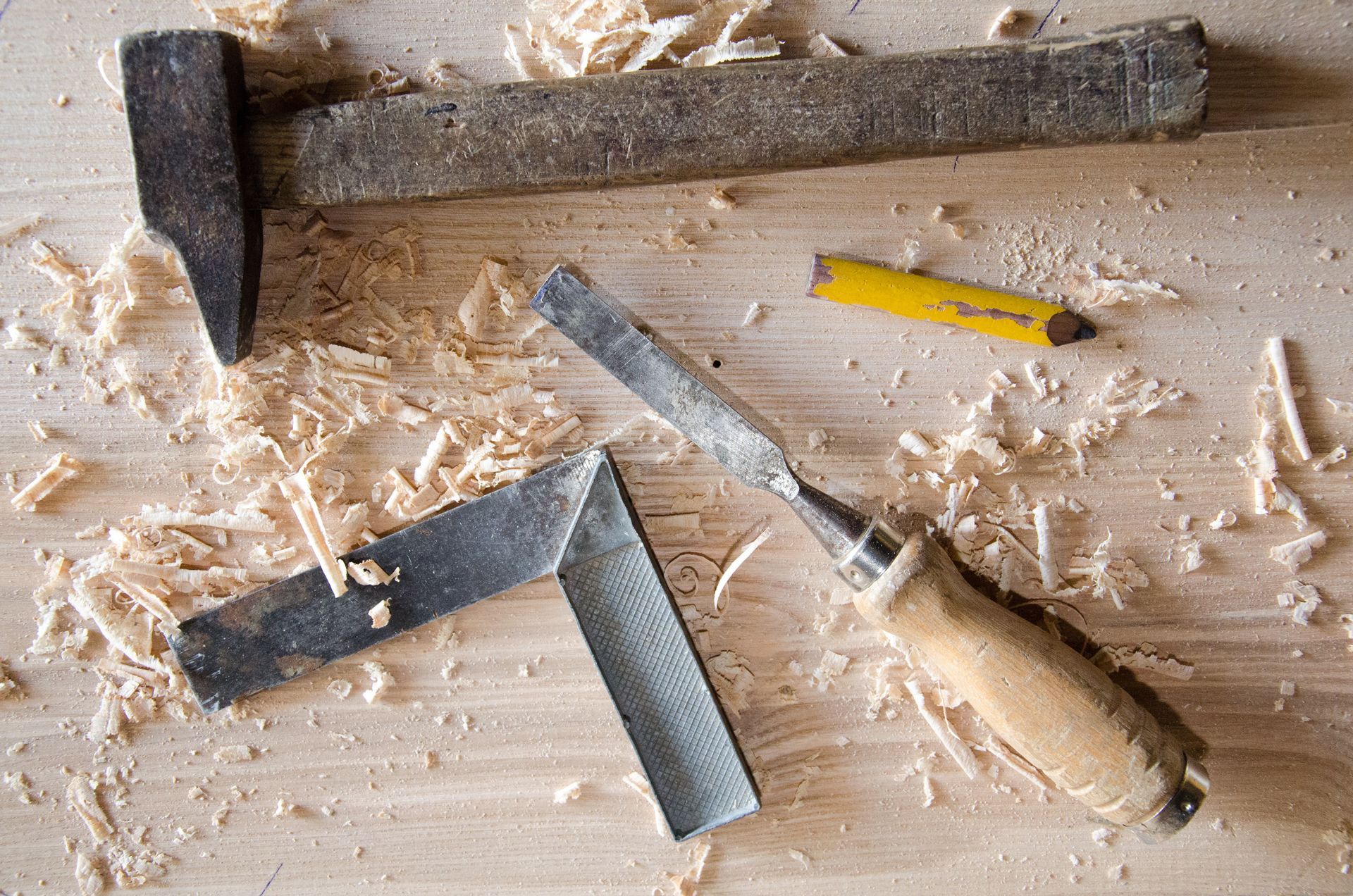 Outils de menuiserie : marteau, ciseau, équerre, crayon et copeaux de bois sur une surface en bois.