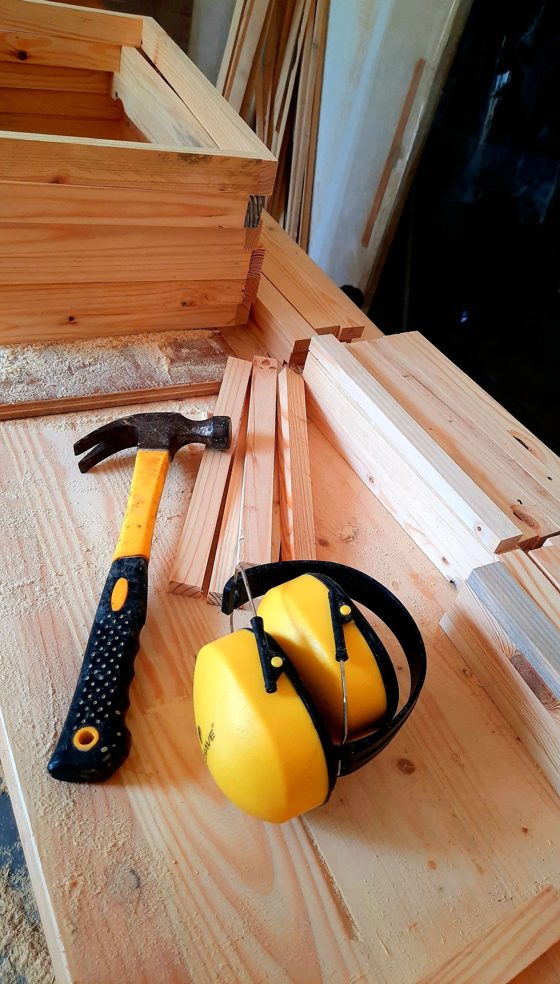 Marteau, morceaux de bois et protection auditive sur une surface en bois, évoquant le travail du bois.