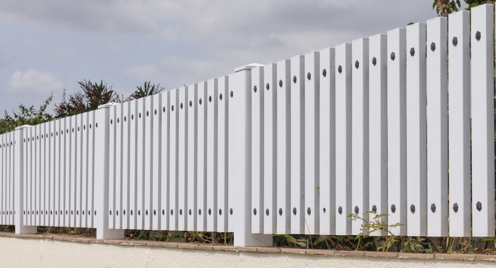 Clôture à lattes verticales blanches, probablement une borne de délimitation, sur un ciel nuageux.
