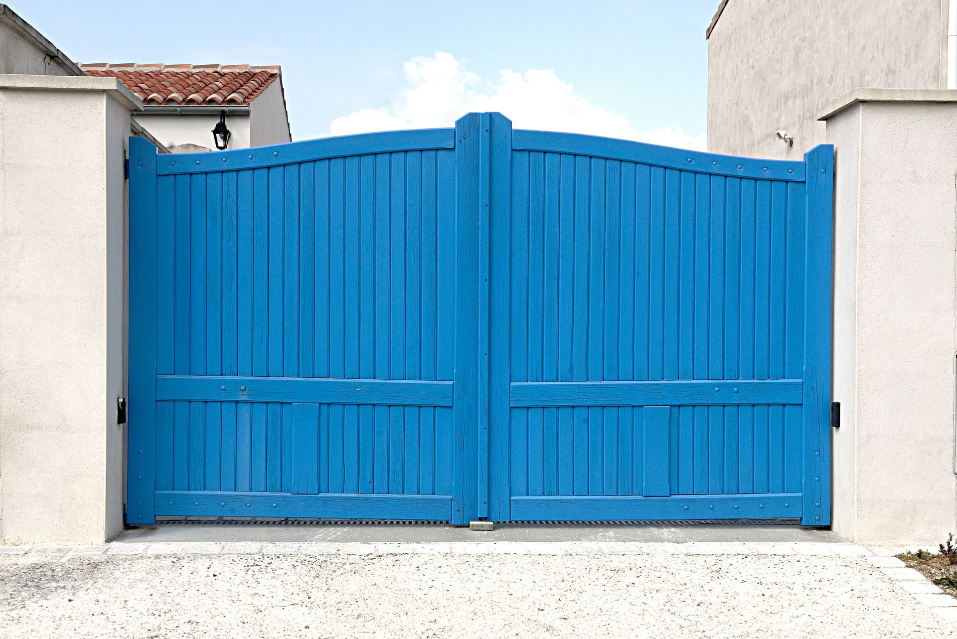 Portail en bois bleu encadré de piliers blancs.