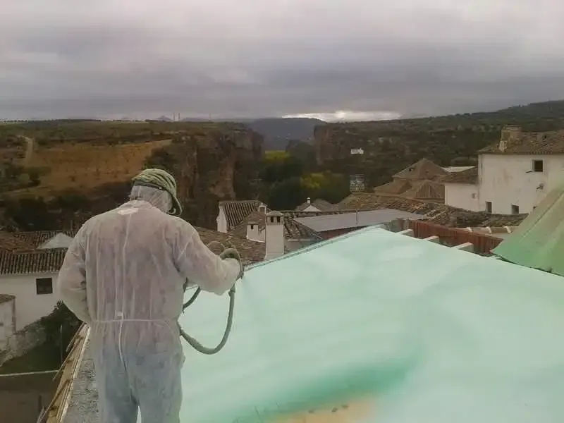 Un hombre está rociando espuma sobre el techo de un edificio.