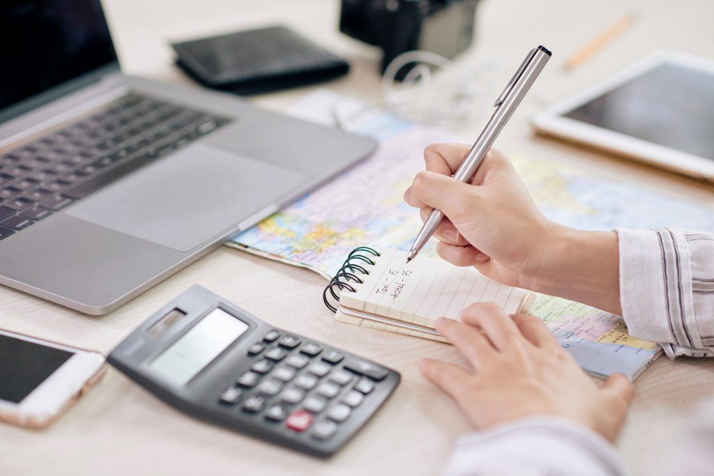 Una persona está escribiendo en un cuaderno al lado de una calculadora y una computadora portátil.