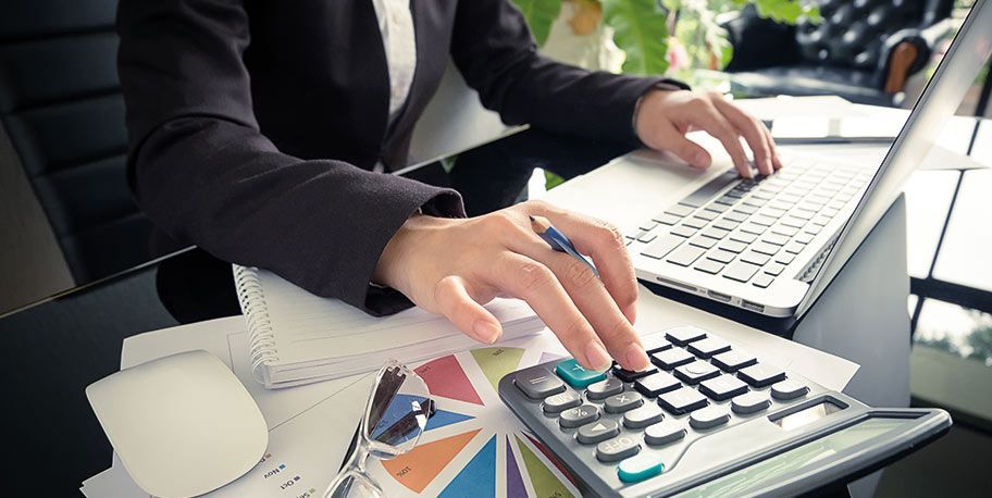 Una mujer está escribiendo en una computadora portátil y usando una calculadora.