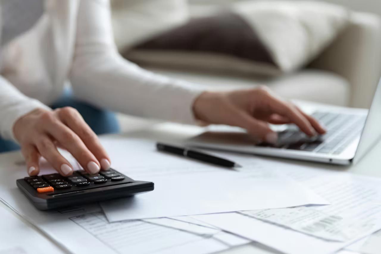 Una mujer está usando una calculadora mientras escribe en una computadora portátil.