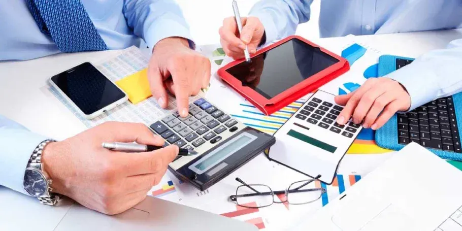 Dos personas están sentadas en una mesa utilizando calculadoras y una tableta.