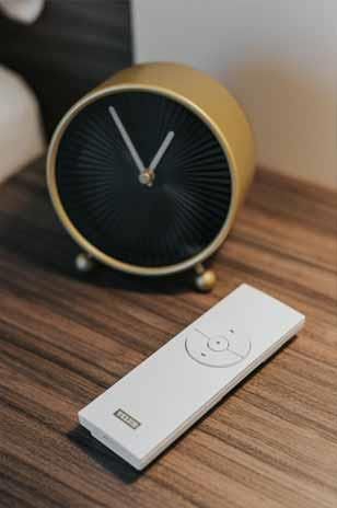 Eine Fernbedienung liegt auf einem Holztisch neben einer Uhr.