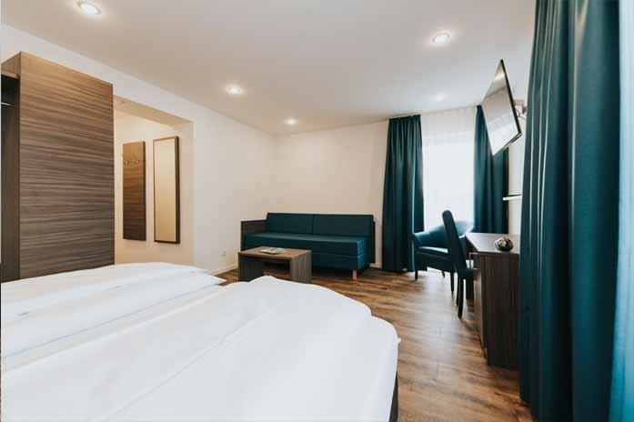 Ein Hotelzimmer mit Bett, Couch, Sessel und Fernseher.