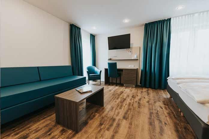 Ein Hotelzimmer mit Couch, Sessel, Schreibtisch und Fernseher.