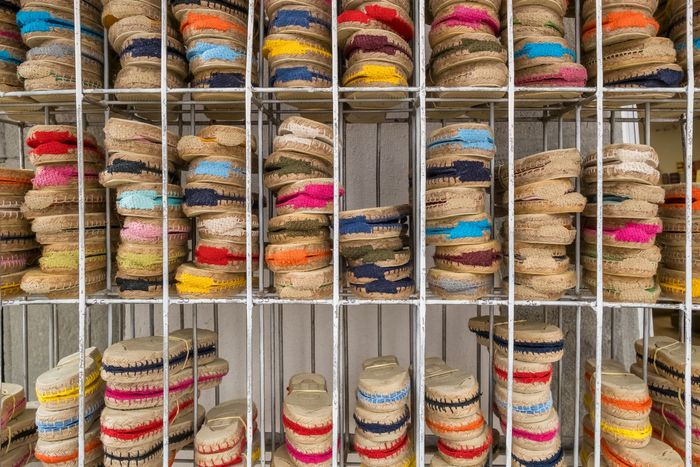 Une étagère métallique grillagée présente des piles d'espadrilles colorées, rangées dans des compartiments individuels.