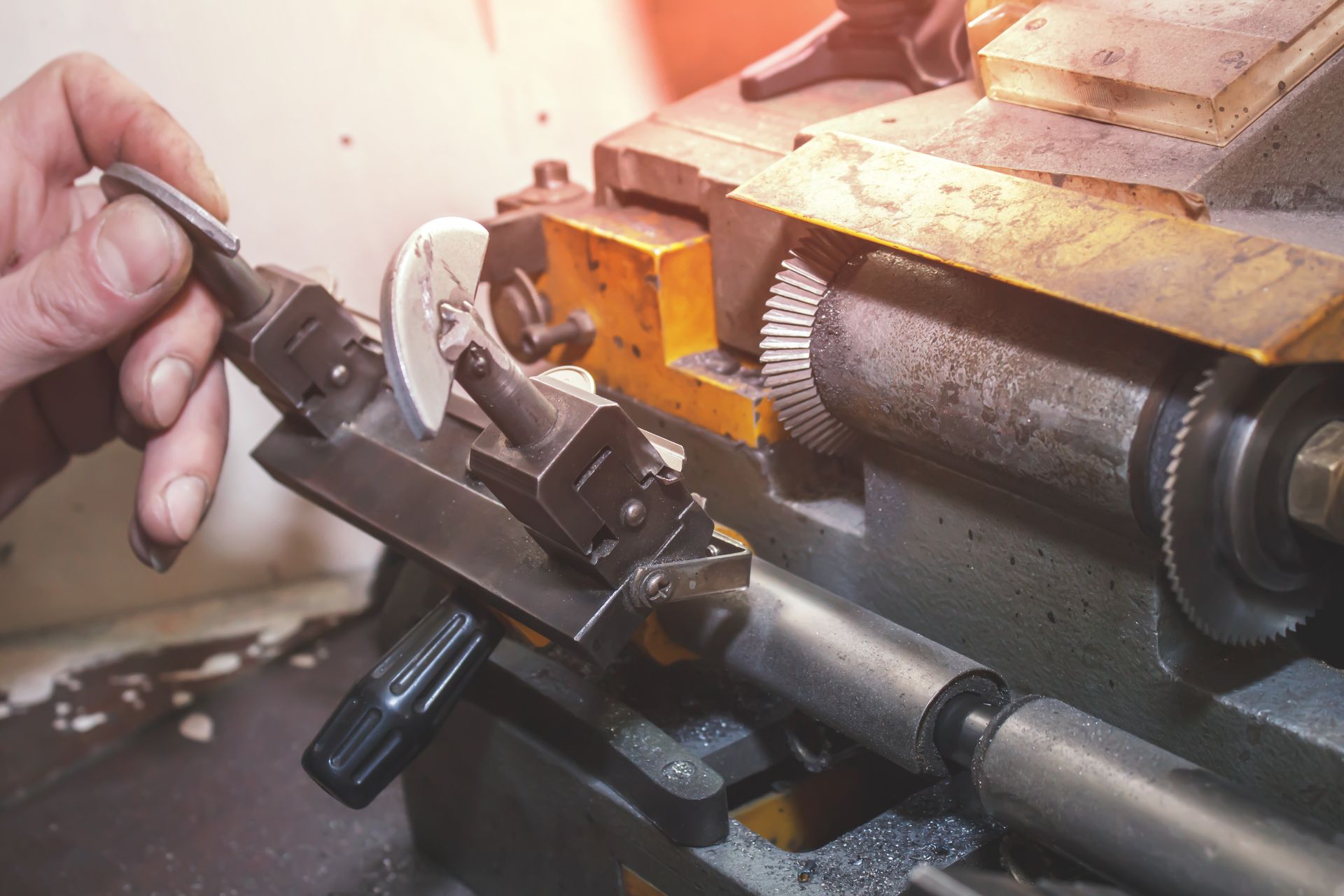 Une main actionne un tour à métaux, ajustant une lame circulaire sur une machine d'atelier mécanique.