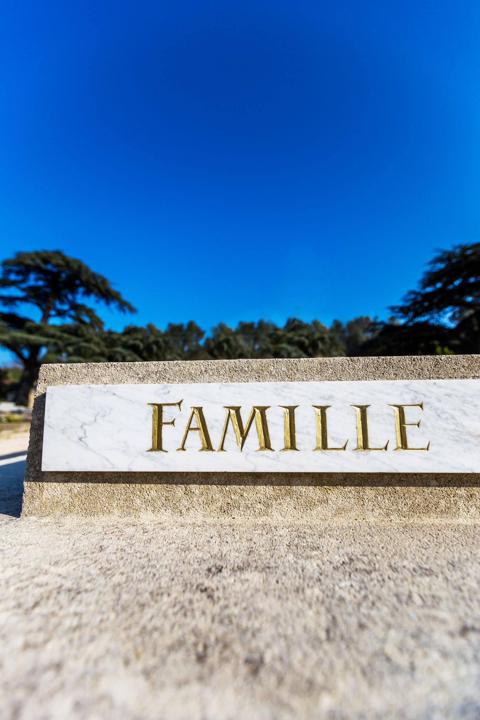 Une plaque de marbre portant l'inscription FAMILLE en lettres dorées, fixée sur un socle en pierre.