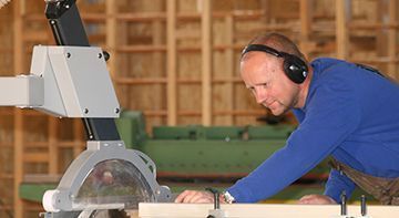 Ein Mann mit Kopfhörern schneidet mit einer Kreissäge ein Stück Holz.