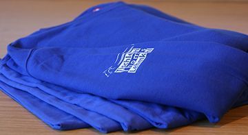 Ein Stapel blauer Hemden mit dem Buchstaben T darauf liegt auf einem Holztisch.