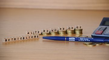 Ein Stift, ein Taschenrechner und ein Stapel Münzen auf einem Holztisch.