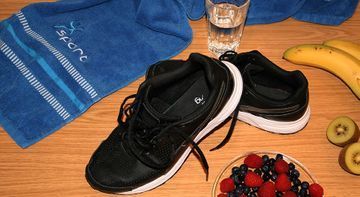 Ein Paar schwarze Turnschuhe stehen auf einem Holztisch neben einer Obstschale und einem Handtuch.